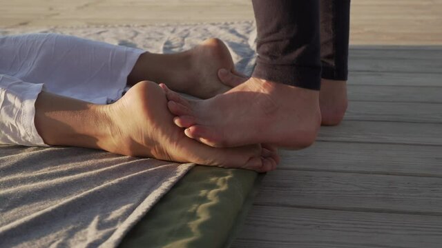 Young female making massage for foot on a wooden floor at sunrise