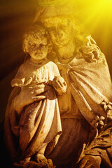 Virgin Mary with Jesus Christ in sunlight. Ancient statue.  Selective focus on faces.