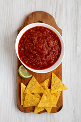 Homemade Tomato Salsa and Nachos on a rustic wooden board on a white wooden table, top view. Flat lay, overhead, from above.