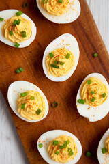 Homemade Deviled Eggs with Chives on a rustic wooden board on a white wooden background, top view. Flat lay, overhead, from above.