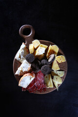 Truffles and cheese on a round wooden Board. Vertical photo on a black background. Top view.