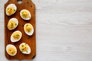 Homemade Deviled Eggs with Chives on a rustic wooden board on a white wooden surface, top view. Flat lay, overhead, from above. Copy space.