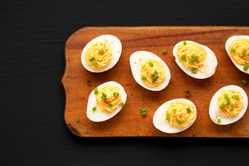 Homemade Deviled Eggs with Chives on a rustic wooden board on a black surface, top view. Flat lay, overhead, from above. Copy space.