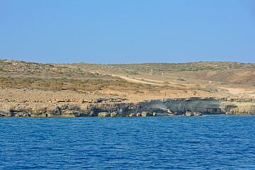 View from the sea on a steep, rocky shore against a clear, blue sky