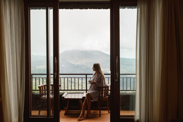 Portrait image of a beautiful woman drinking hot coffee on balcony with mountains view