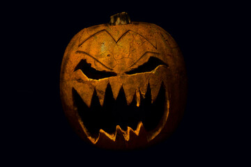 
A spooky halloween pumpkin with evil face and eyes in black color on black isolated background
