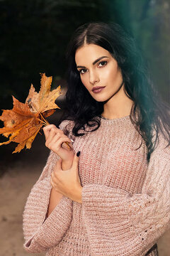 Portrait of a woman in an autumn park with maple leaves in her hands
