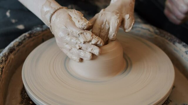 Close-up of dirty kid's hands working with wet clay on throwing wheel shaping pot busy with creativy activity in crafts class. Childhood and arts concept.