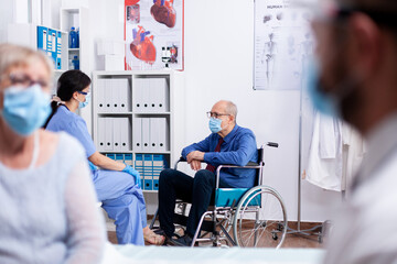 Disabled old man sitting in wheelchair wearing face mask agasint coronavirus while talking with...