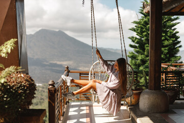 Positive caucasian woman sits in hanging chair  with view on the lake Batur. Travel Bali concept