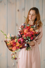 young woman florist in a pink dress with red hair holds a wedding bouquet of flowers roses
