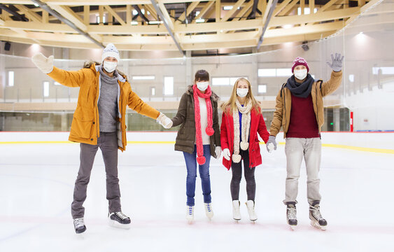 people, friendship, gesture, sport and leisure concept - friends wearing face protective medical masks for protection from virus disease waving hands on skating rink