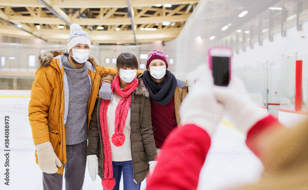 Poster people, friendship, technology and leisure concept - friends wearing face protective medical masks for protection from virus disease taking photo with smartphone on skating rink