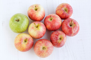 Top view of several red apples and one green apple on an old white wooden table