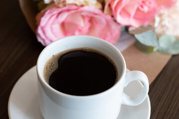 A cup of black hot coffee and a lovely bouquet of roses