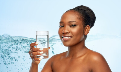 beauty and people concept - portrait of happy smiling young african american woman with glass of water over blue background with bubbles in water splash