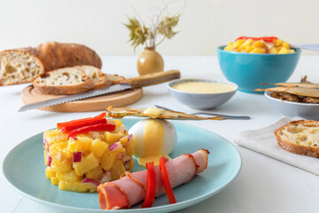 Henri Egg, tasty brunch or snack. Boiled eggs and smoked sprats fish with mayonnaise, ham and potato salad. White wooden table, no people.