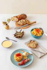 Henri Egg, tasty brunch or snack. Boiled eggs and smoked sprats fish with mayonnaise, ham and potato salad. White wooden table, no people.