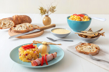Henri Egg, tasty brunch or snack. Boiled eggs and smoked sprats fish with mayonnaise, ham and potato salad. White wooden table, no people.