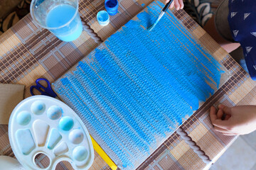 the girl draws blue gouache cardboard, makes a background, sits in the home kitchen