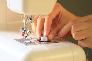 Preparing the sewing machine for work. Seamstress tucks thread into the eye of a needle. Installs the bobbin in the shuttle. Close up view.