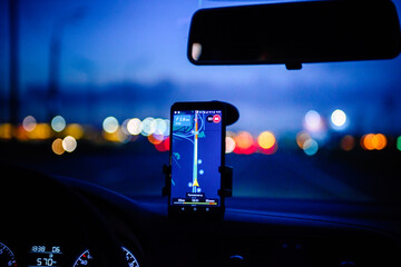 Smartphone with map on the screen in car. Automobile dashboard in night mode.