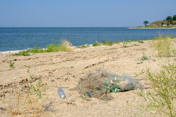 Fototapeta na wymiar Sandy beach next to the sea on a summer sunny day. On the sand lies a tangled fishing net. The result of the activity of poachers. Nature protection concept.