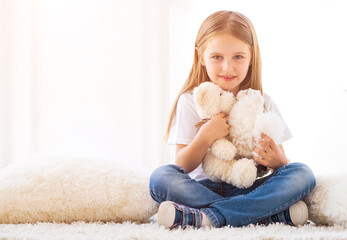 Cute girl hugging toys sitting on carpet in her room