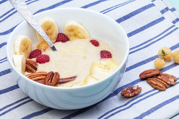 Delicious amaranth with butter, fresh raspberries and banana, pecans and almond chips. Plant-based breakfast. Healthy colorful gluten free concept.