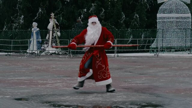 Russian Ded Moroz like a Santa Claus dances on city square near the Central Christmas tree. New year concept. Discounts and promotions, sales. Funny and comic situation