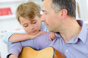 Man playing guitar, child leaning on his shoulder