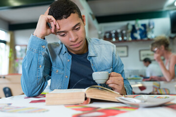 young man alone at cafe table reading book