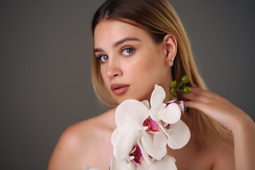 Adorable young girl with perfect makeup. Photo of blonde girl with orchids on a gray background. Skin care concept