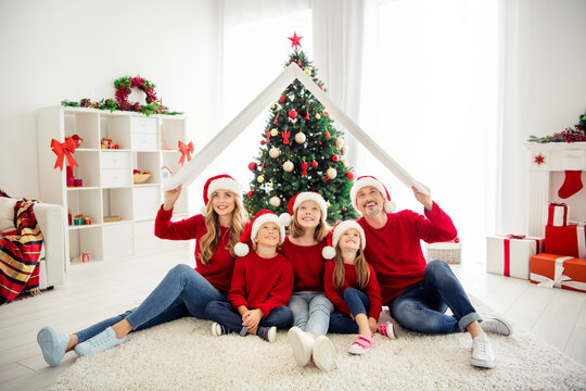 Portrait photo of brother and sisters spending winter time with parents. Two daughters and son smiling looking up sitting near decorated xmas tree present boxes at home
