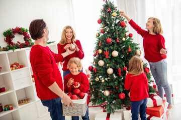 Photo of full big family five people gathering three small kids decorate x-mas tree dad hold box give ball mom son wear red jumper jeans in home living room presents mistletoe indoors