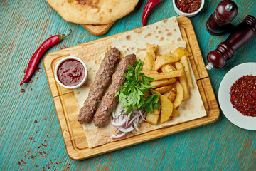 Classic Oriental grilled in bbq lula kebab with red sauce and side dish of baked potatoes. Eastern cuisine