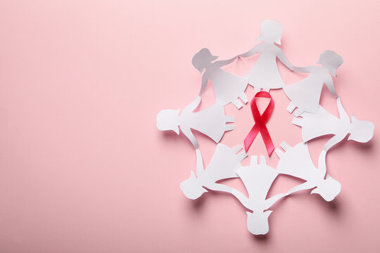 Paper women and awareness ribbon on pink background, top view
