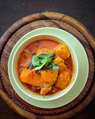 Chicken curry in a green bowl on a wooden base background.