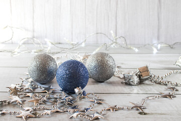 Three Christmas balls and a garland of silver stars on a light background and space for design.