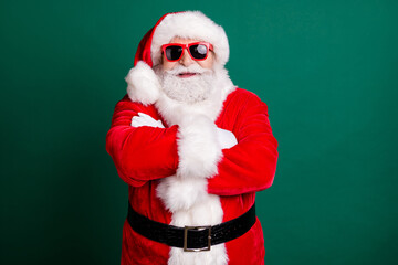 Photo of retired grandpa white beard crossed arms confident look wait decoration christmas tree wear red santa costume coat gloves belt sunglass headwear isolated green color background