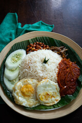 Traditonal Malaysia Asian food Nasi Lemak on a banana leaf in a wooden bamboo plate.