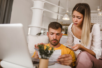 Portrait of young couple paying bills online using laptop and credit card.