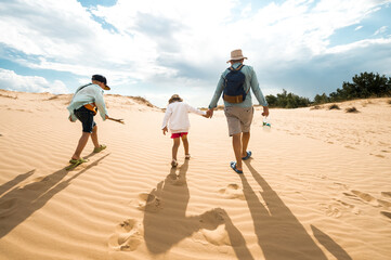 Fototapeta premium Man and kids boy and girl walk through desert in Oleshky Sands, Kherson region, Ukraine. The largest desert in Europe. People with backpack and water in bottle
