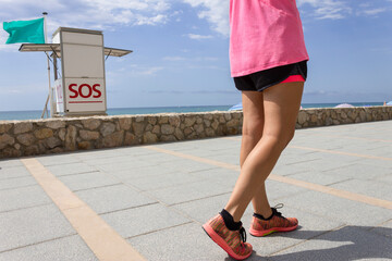Fitness woman walking in promenade ,next to life guard tower on the beach. Before or after running workout.Concept of sport and healthy lifestyle.