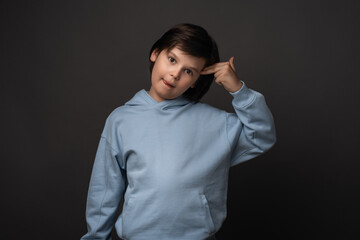 Perplexed boy 10-12 years old point fingers to head as if he about shoot self. Studio shot, gray background
