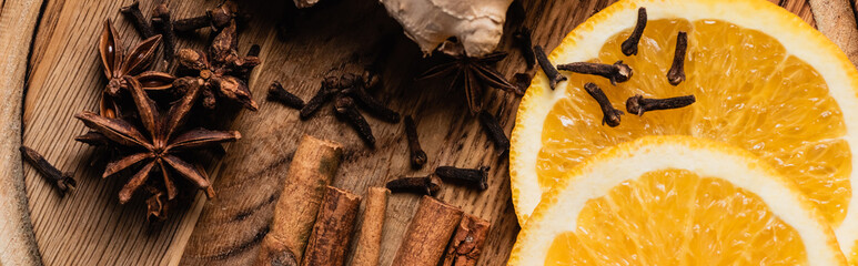 Panoramic shot of orange slices and spices on wooden background