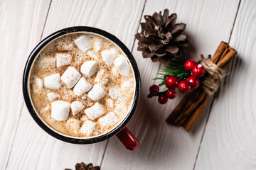 Top view of cup of cocoa near cinnamon sticks and pine cone on wooden background