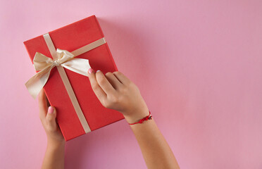 Gift box on an isolated pink background. Rectangular gift box. Woman's hands grabbed the box.