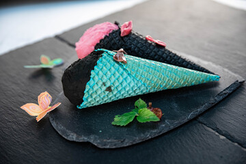 Black ice cream in a blue waffle cone on a black background decorated with flowers