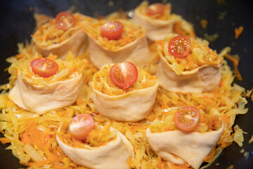 Rolls of dough with cabbage filling and cherry tomatoes cooked in a cast iron pan